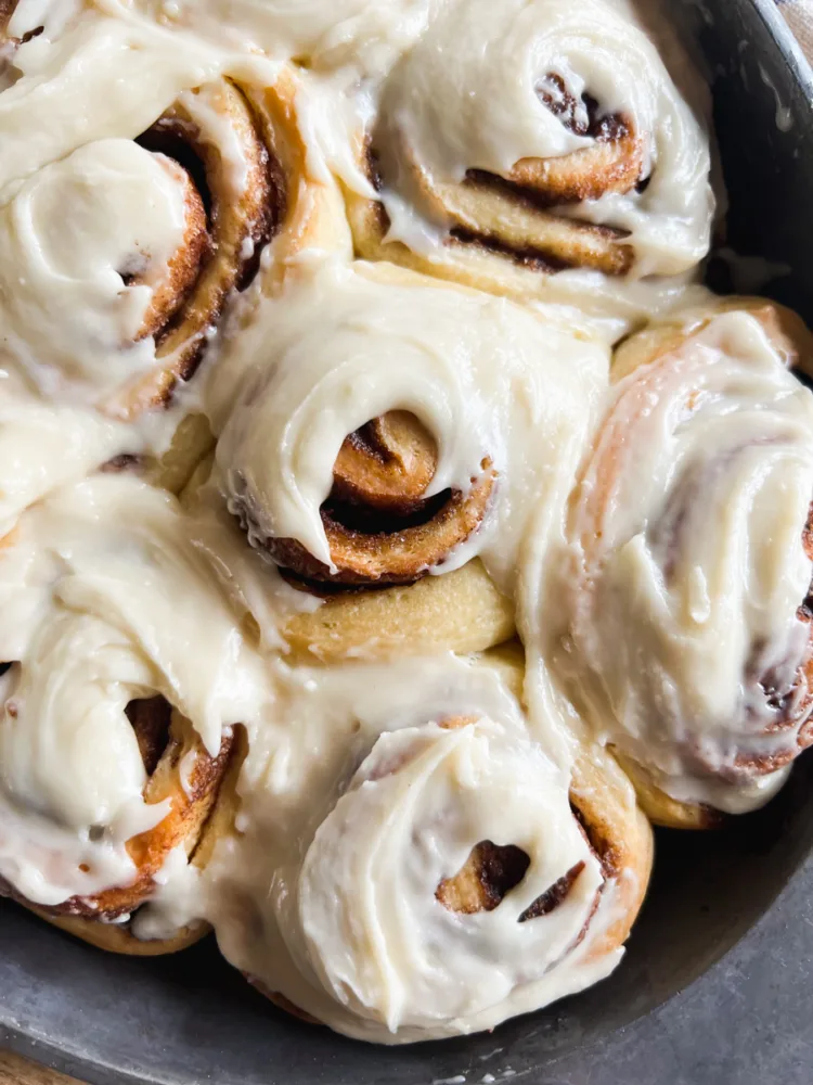 Freshly baked sourdough cinnamon rolls with a soft, pillowy texture and a thick layer of creamy frosting.