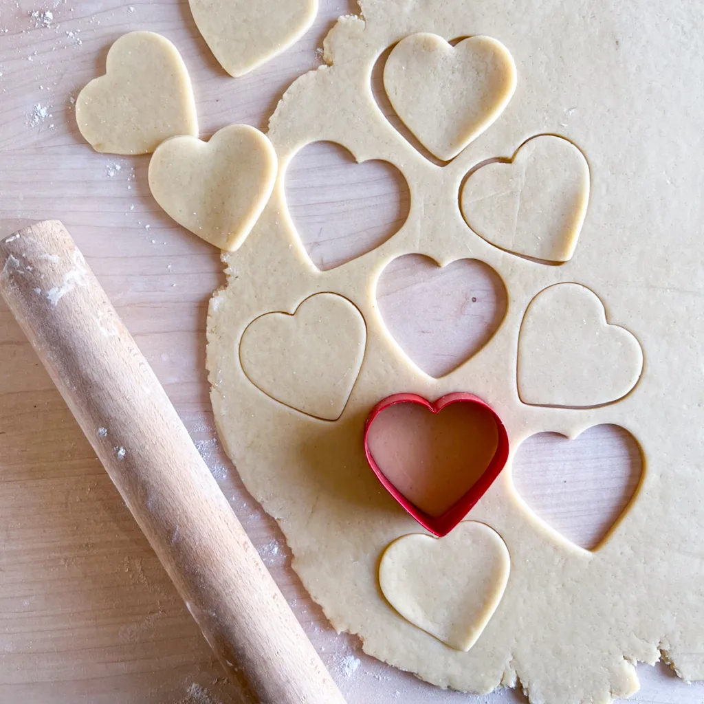 Rolled sourdough sugar cookie dough being cut into heart shapes.