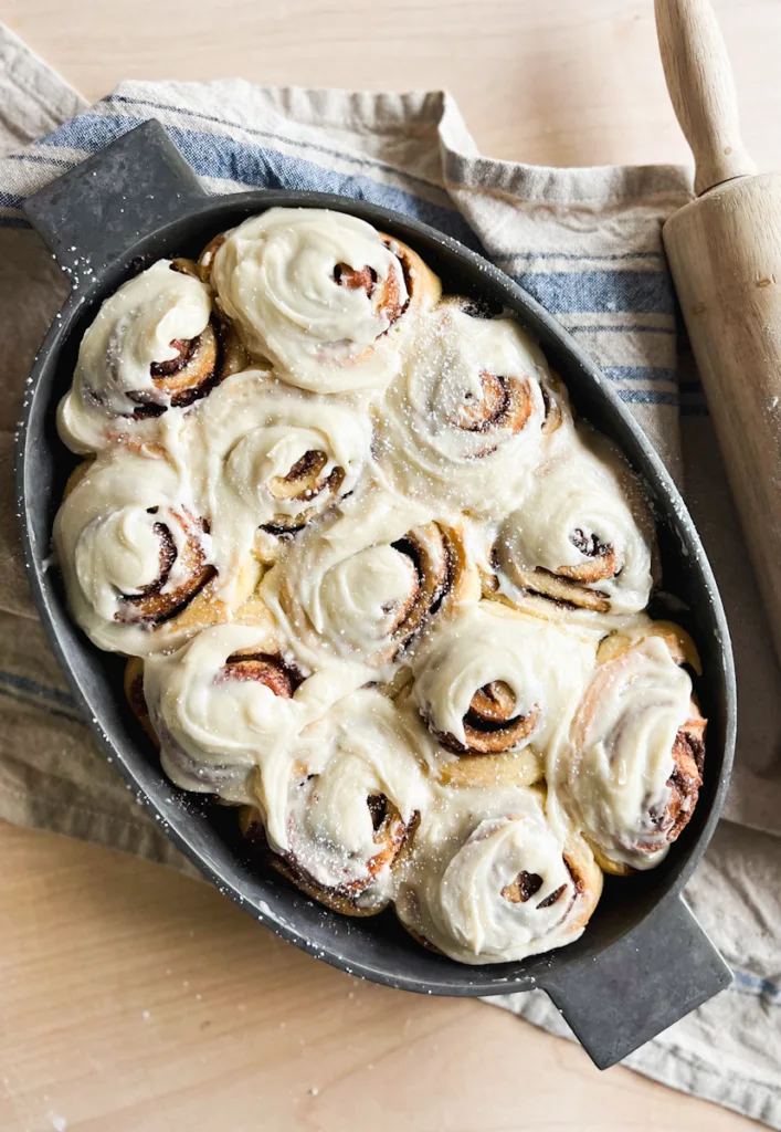 A pan of frosted sourdough cinnamon rolls next to a rolling pin