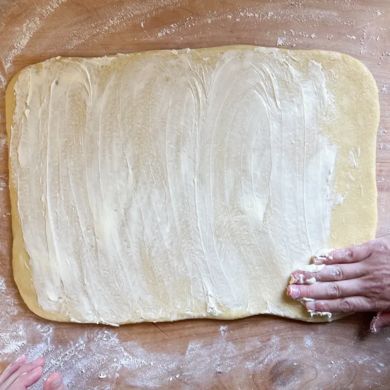 Butter being spread over the brioche dough for brioche cinnamon rolls.