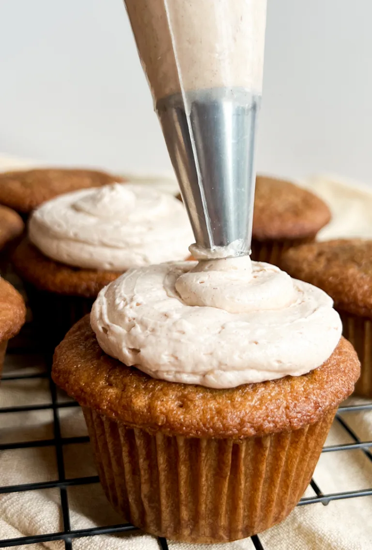 A cinnamon cupcake being frosted with cinnamon buttercream frosting.