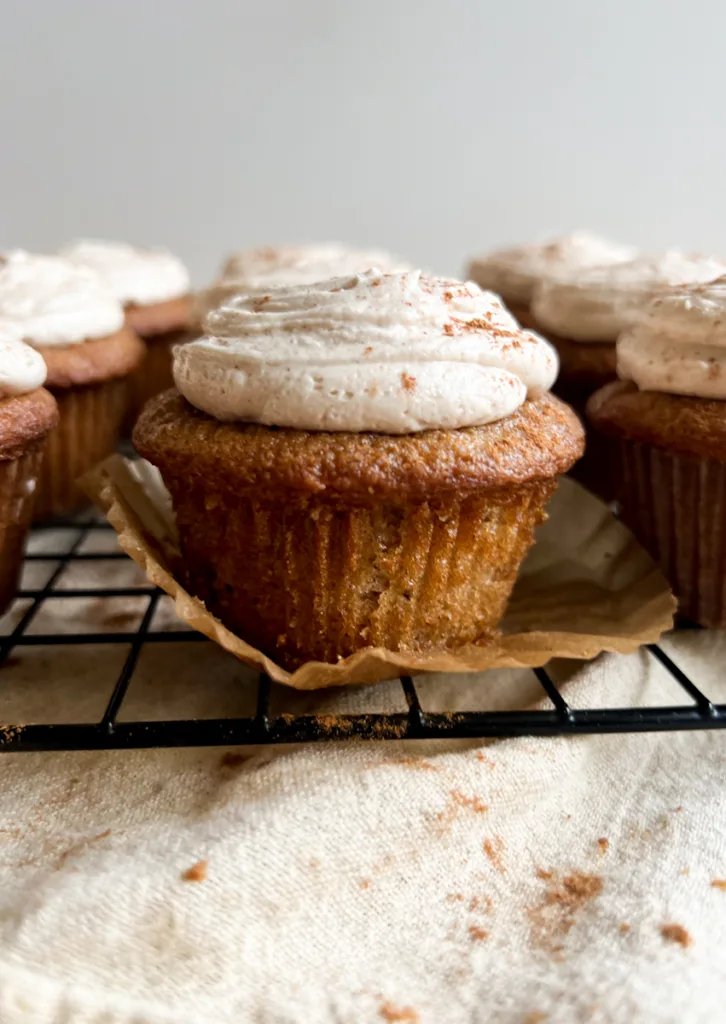 A cinnamon cupcake sitting on a cooling rack with its paper peeled off.