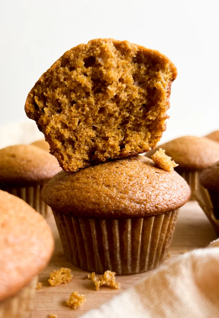A stack of sourdough pumpkin muffins with the top one ipped in half to show the inside texture.