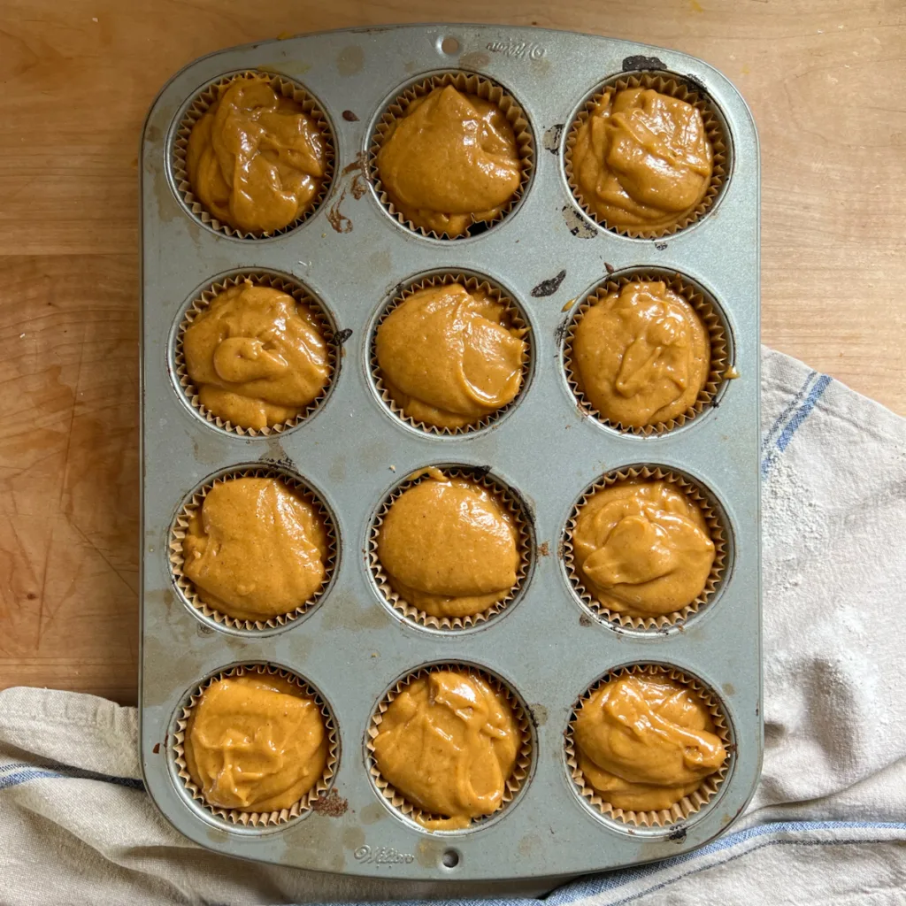 A tray with muffin cups filled with sourdough pumpkin muffin batter.