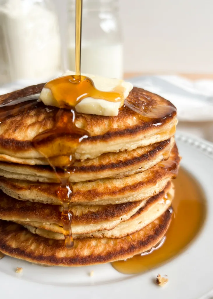 Sweet cream pancakes with syrup being poured over them.