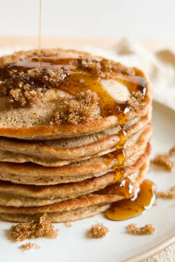 A stack of cinnamon brown sugar pancakes with maple syrup on top.