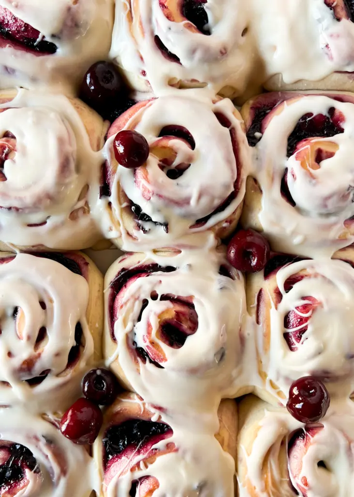 A pan of cherry cinnamon rolls topped with cream cheese icing.