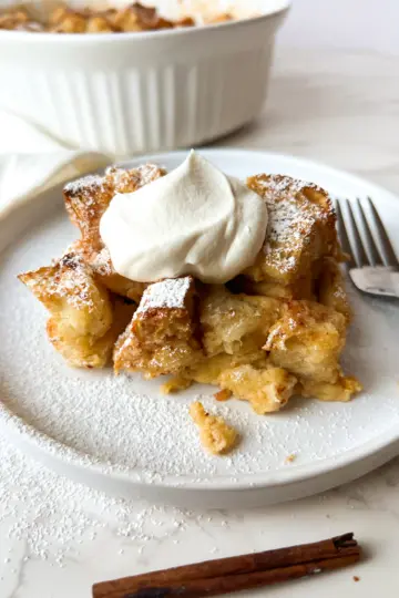 A slice of eggnog bread pudding on a plate topped with whipped cream.