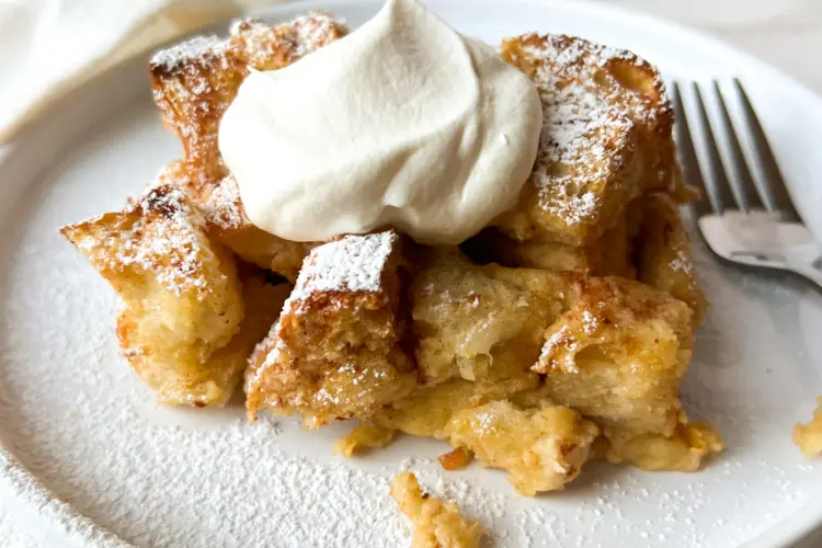 A slice of eggnog bread pudding on a plate topped with whipped cream.