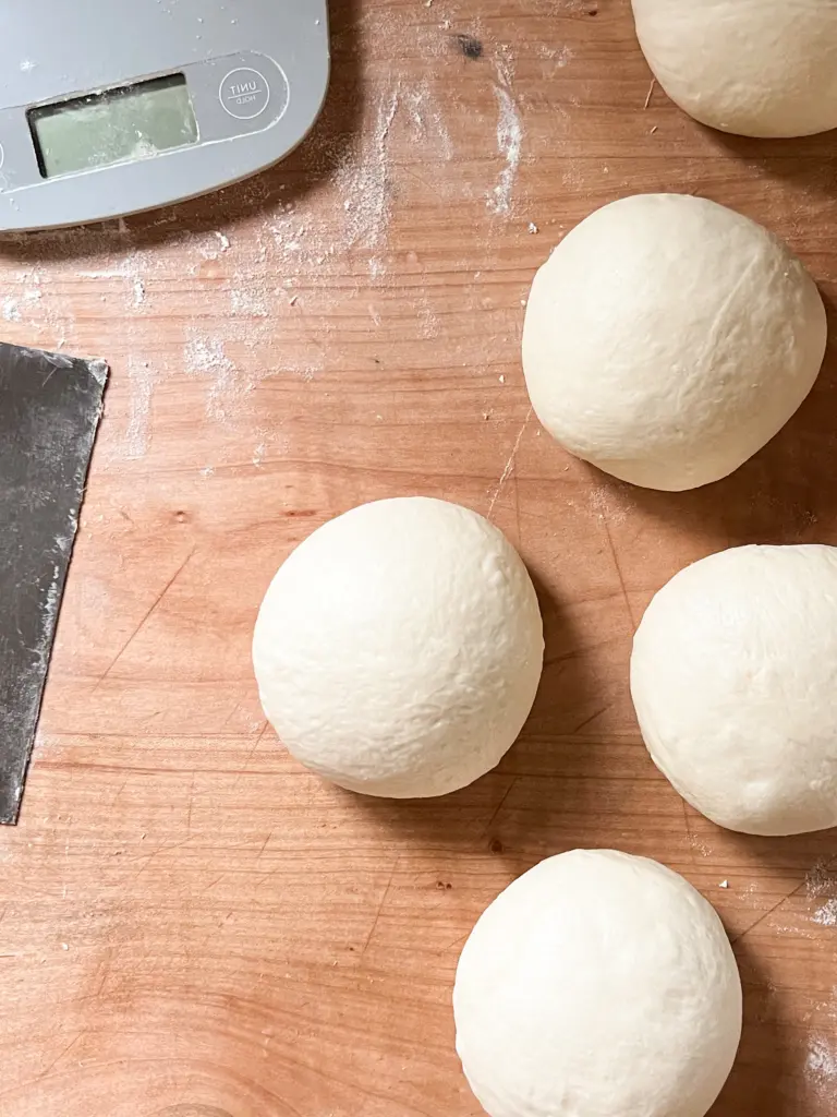 Dough balls after having been shaped sitting next to each other on a dough bord.