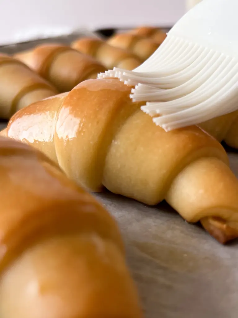 A sourdough crescent roll being brushed with butter.