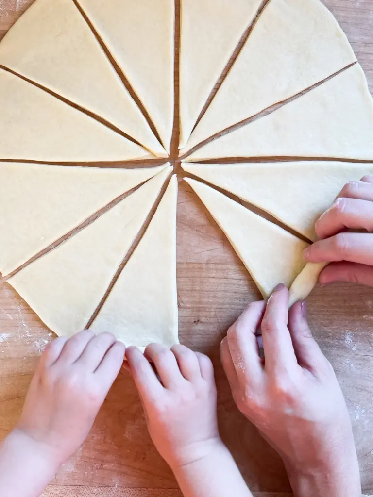 Two sets of hands, one mother and one child, rolling up the wedges into crescent shapes.