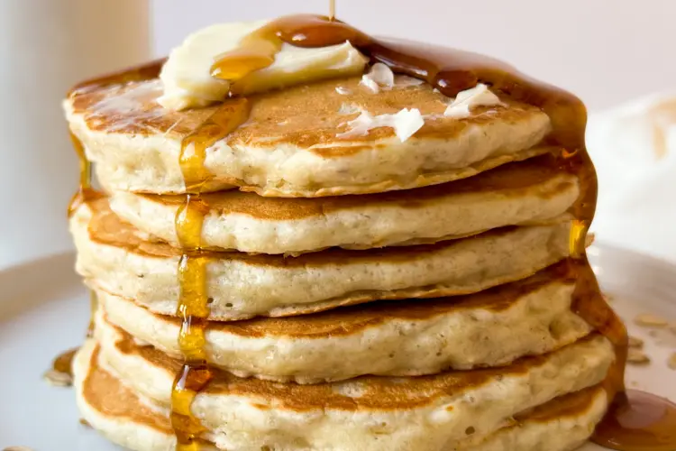 A stack of sourdough oatmeal pancakes with syrup being poured on top.