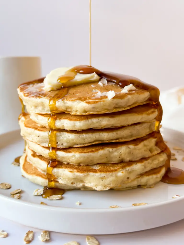 A stack of sourdough oatmeal pancakes with syrup being poured on top.