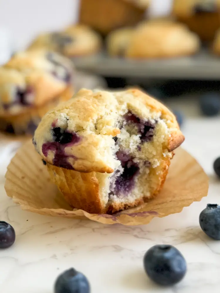 A blueberry buttermilk muffin with a bite taken out of it.