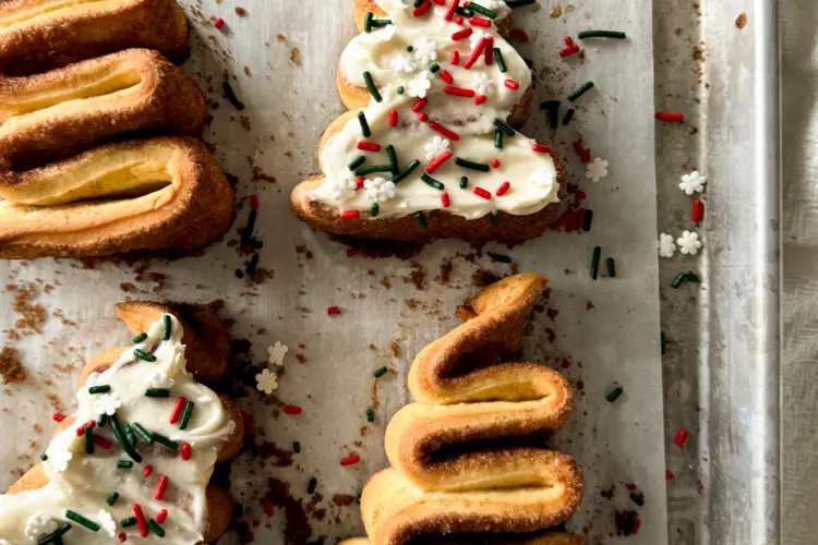 A tray of frosted Christmas tree cinnamon rolls topped with festive sprinkles.