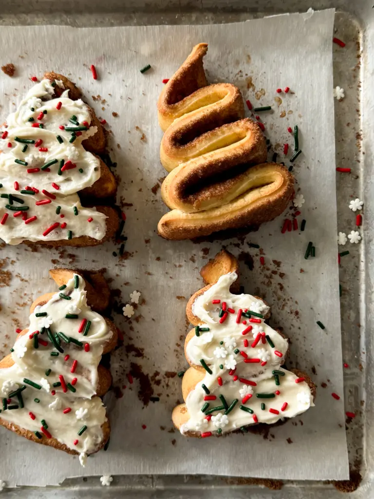 A tray of frosted Christmas tree cinnamon rolls topped with festive sprinkles.