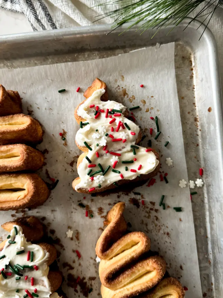 A tray of frosted Christmas tree cinnamon rolls topped with festive sprinkles.