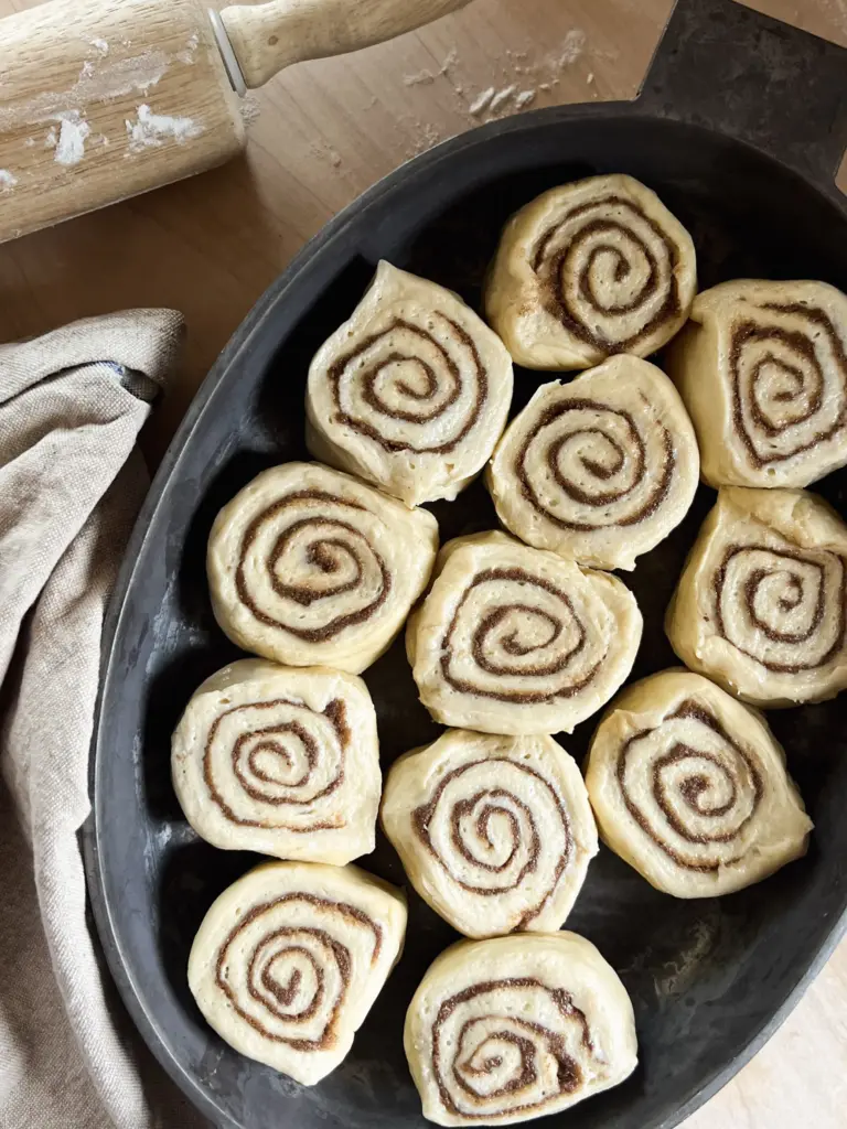 Freshly cut sourdough cinnamon rolls placed in a pan, showing their soft dough and cinnamon-sugar swirls before proofing.