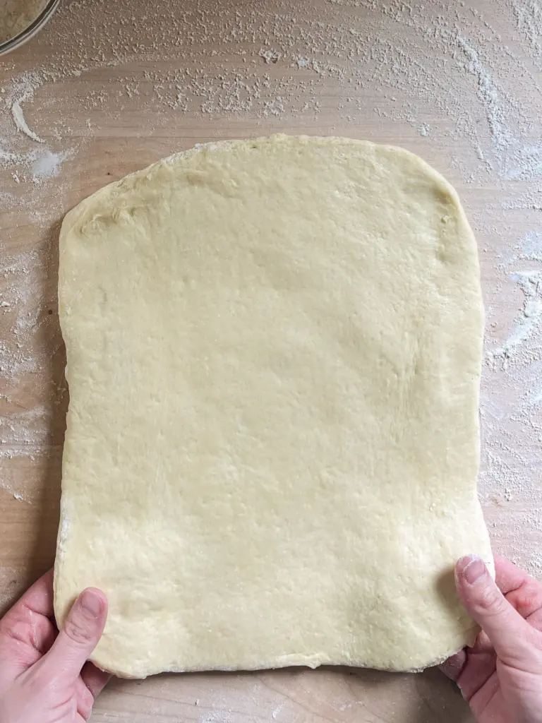 Sweet sourdough cinnamon roll dough rolled out evenly on a floured work surface, ready for cinnamon sugar filling.