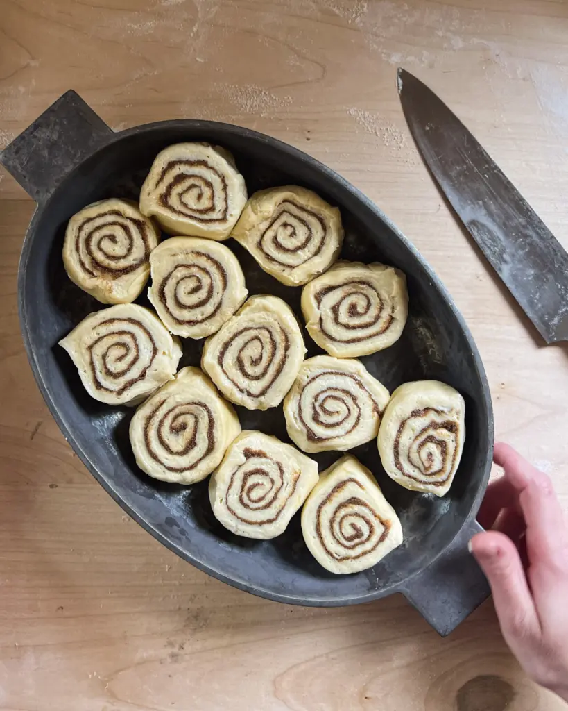 Freshly cut sourdough cinnamon rolls arranged in a baking pan, ready for their final proof before baking.