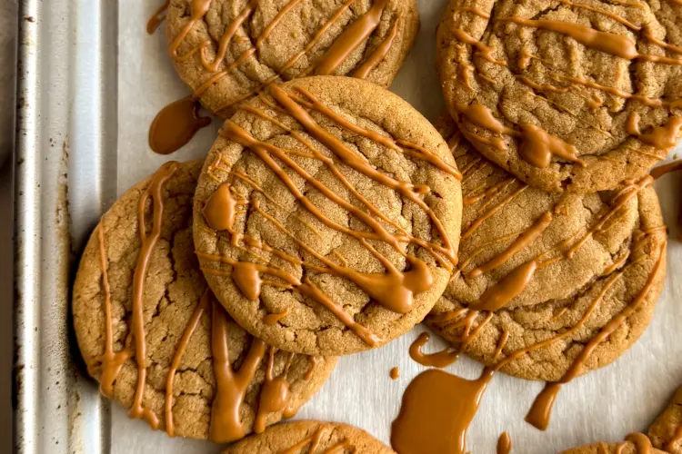 Overhead view of a batch of biscoff cookie butter cookies cooling on a parchment lined baking sheet.
