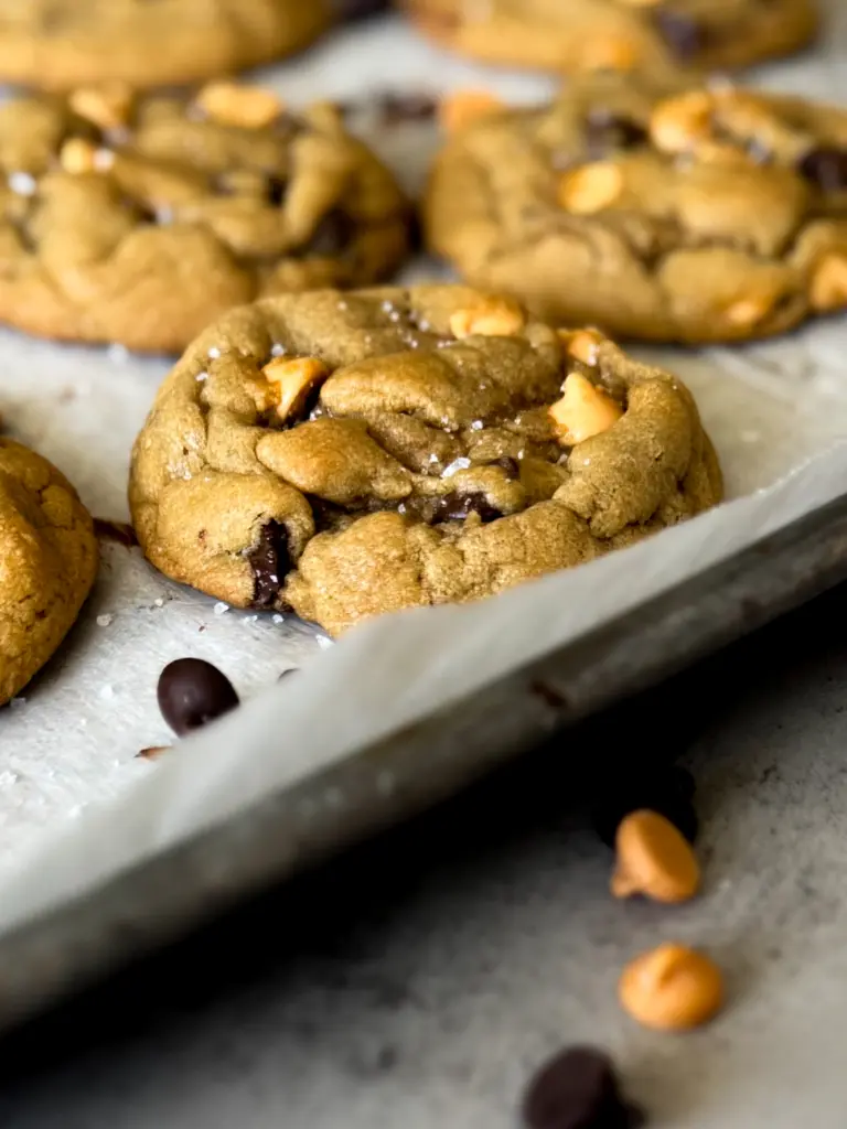 Chewy chocolate chip butterscotch cookies sprinkled with flakey sea salt on a parchment-lined baking sheet.