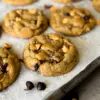 Chewy chocolate chip butterscotch cookies sprinkled with flakey sea salt on a parchment-lined baking sheet.